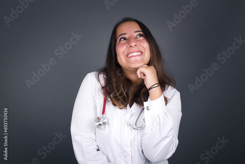 portrait of mysterious charming blonde female with straight hair looking up with enigmatic smile. Beautiful smiling girl looking up standing against gray wall.