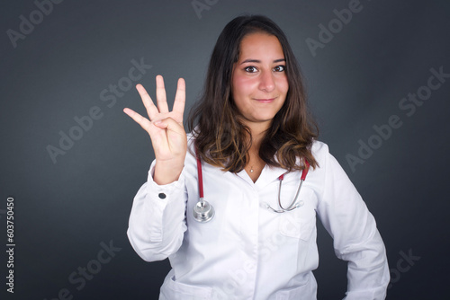 Young woman standing against gray wall showing and pointing up with fingers number four while smiling confident and happy.