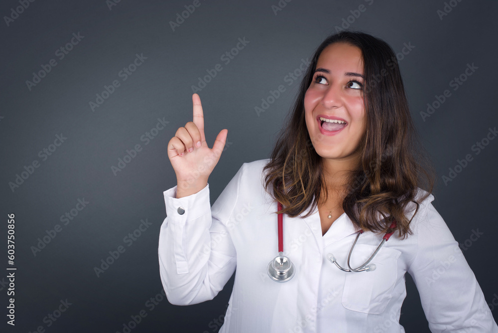 Close up portrait of pleasant looking doctor woman has clever expression, raises one finger, remembers herself not to forget tell important thing. Indoors Close up portrait of pleasant looking doctor woman has clever expression, raises one finger, remembers herself not to forget tell important thing. Indoors