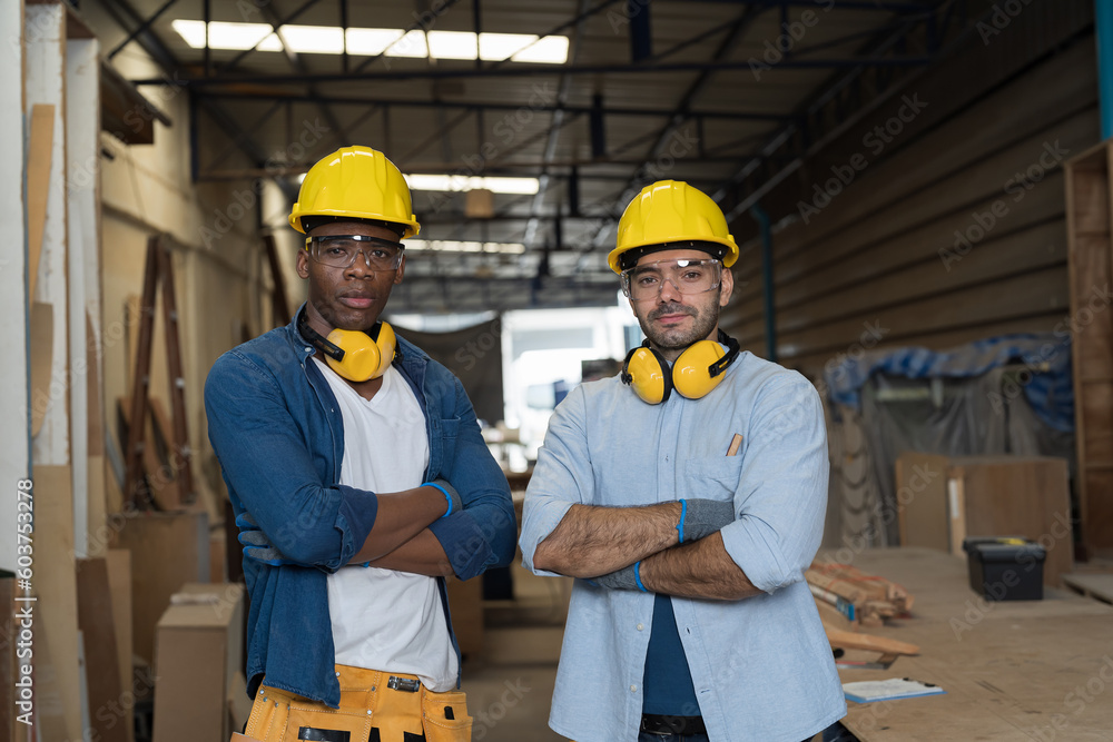 Portrait of two male carpenter working in wood workshop. Group of male joiner wearing safety uniform, gloves, helmet and working in furniture workshop Portrait of two male carpenter working in wood workshop. Group of male joiner wearing safety uniform, gloves, helmet and working in furniture workshop