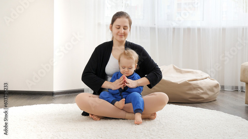 Beautiful young mother with her baby son sitting on floor and meditating. Family healthcare, active lifestyle, parenting and child development