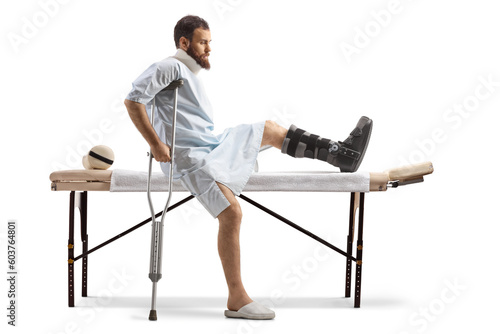 Man in a hospital gown sitting at a medical table with a broken leg and neck collar