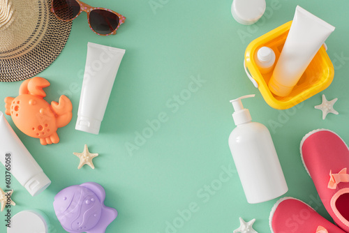 Baby sun protection concept. Top view flat lay of sunscreen bottles, beach toys, sunhat, baby beach shoes, sunglasses and starfish on teal background with space for text or advert