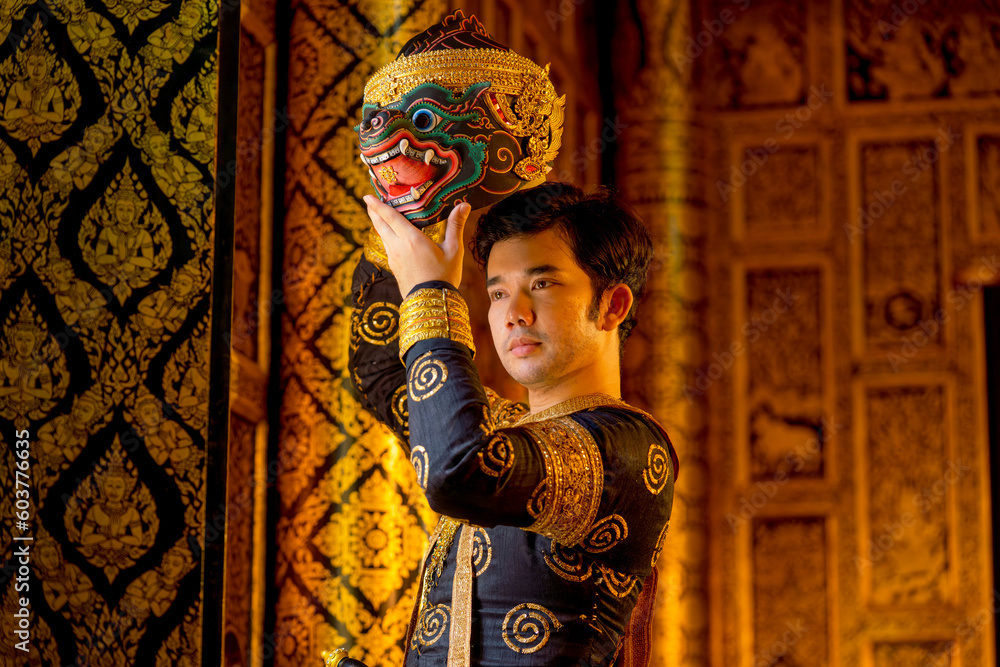 Fototapeta premium Asian man with traditional cloth relate to Khon or Thai classic masked with holding black monkey mask stand in front of windows of public building.