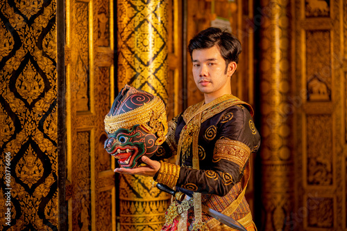 Asian man with traditional cloths relate to Khon or Thai classic masked stand with holding black monkey mask in front of windows of public building also look at camera.