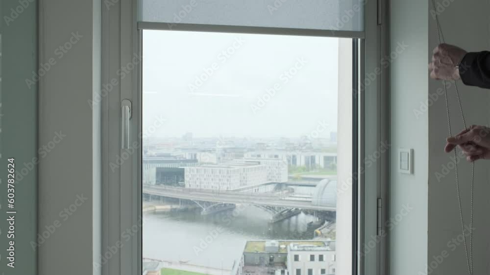 closing a gray fabric roller shade at a window in a skyscraper office building closing a gray fabric roller shade at a window in a skyscraper office building