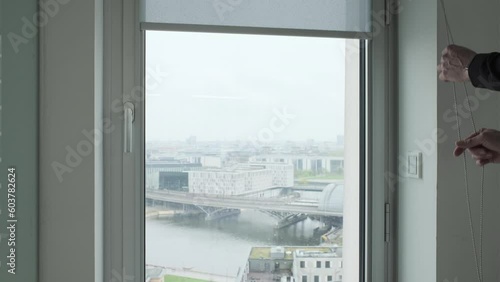 closing a gray fabric roller shade at a window in a skyscraper office building
