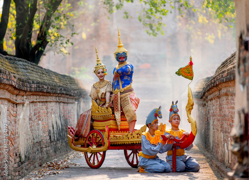 Khon Thai classic masked from the Ramakien with characters of woman and blue monkey stay together on traditional chariot in front of ancient building with mist or fog.