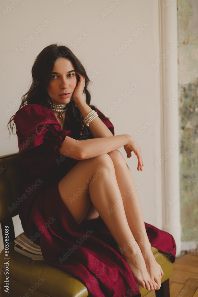Girl in the cherry dress sitting on green chair. Women's health, sexuality. Portrait of a beautiful young woman in cherry dress with belt and puff sleeves. Sexy brunette woman look sensual. Girl in the cherry dress sitting on green chair. Women's health, sexuality. Portrait of a beautiful young woman in cherry dress with belt and puff sleeves. Sexy brunette woman look sensual.