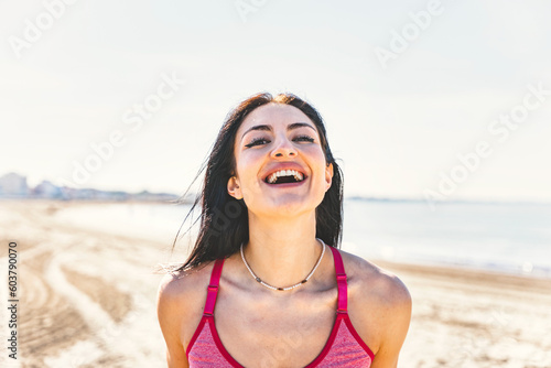 Happy caucasian young sporty woman smiling at camera outdoors on the beach- Close up portrait of healthy girl laughing after training- Sport Lifestyle and body positive concept 