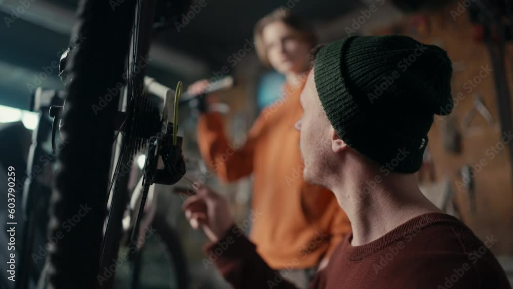 Dad and son work in the garage: dad teaches son how to fix a bike. Dad spins the wheel to see if the bike is working Dad and son work in the garage: dad teaches son how to fix a bike. Dad spins the wheel to see if the bike is working