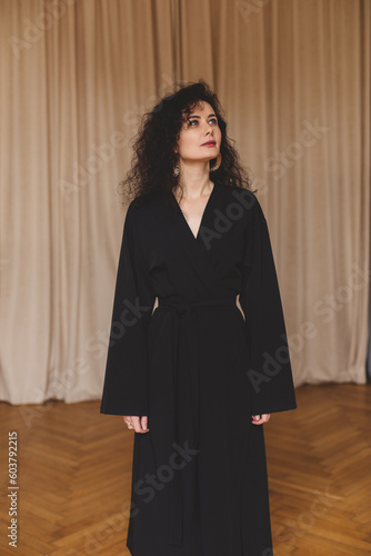 Woman wear black kimono and earrings. The girl dress in robe look seductively. Fashionable details of kimono. Relax style woman with curly hair at home.