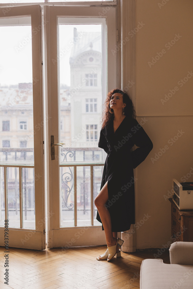 Woman wear black kimono and earrings. The girl dress in robe look seductively. Fashionable details of kimono. Relax style woman with curly hair at home. Woman standing near door on balcony.