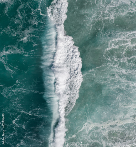 Aerial view of a strong wave crashing with surfers nearby 