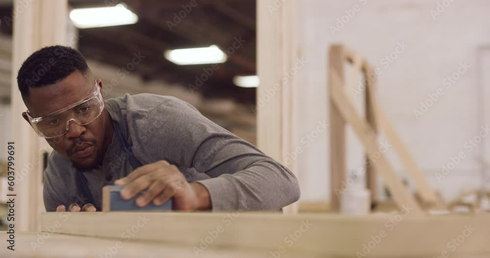 Carpentry, design and focus with a black man sanding a plank in a factory for professional woodwork. Safety goggles, manual labor and expertise with a serious male carpenter working in his workshop Carpentry, design and focus with a black man sanding a plank in a factory for professional woodwork. Safety goggles, manual labor and expertise with a serious male carpenter working in his workshop