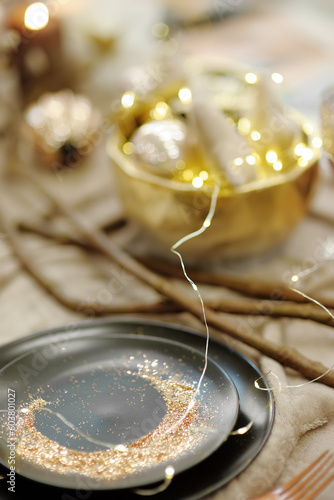 Stylish table set with black crockery, golden sand and original lights for wedding reception. Trendy wedding party
