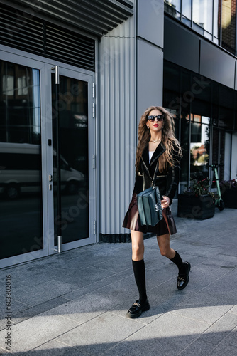 glamorous lady with long legs in a black jacket walking down the city street 