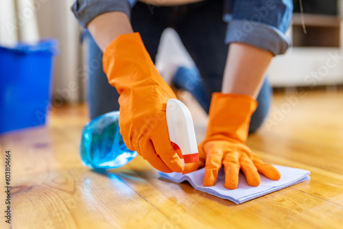 Woman in rubber gloves wiping up dust with spray and rag while cleaning floor