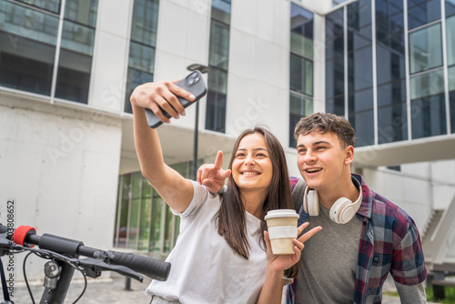 Two teenagers standing with skateboard and electric scooter looking at mobile phone making selfies or a video call, modern lifestyle concept