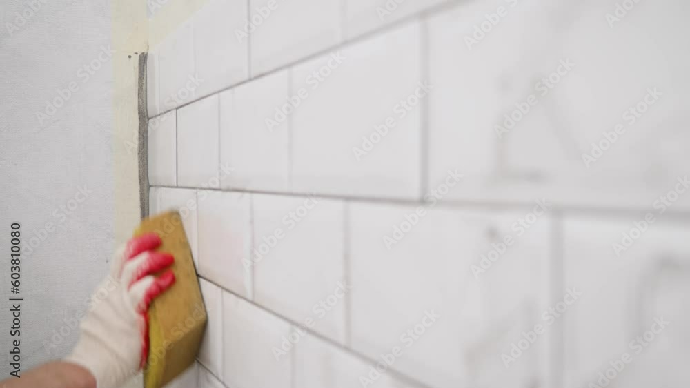 The tiler wipes the tiles after laying, professional highly qualified technology for laying and finishing tiles. Close-up of rubbing with a sponge after the process of grouting cracks on a tiled wall. The tiler wipes the tiles after laying, professional highly qualified technology for laying and finishing tiles. Close-up of rubbing with a sponge after the process of grouting cracks on a tiled wall.