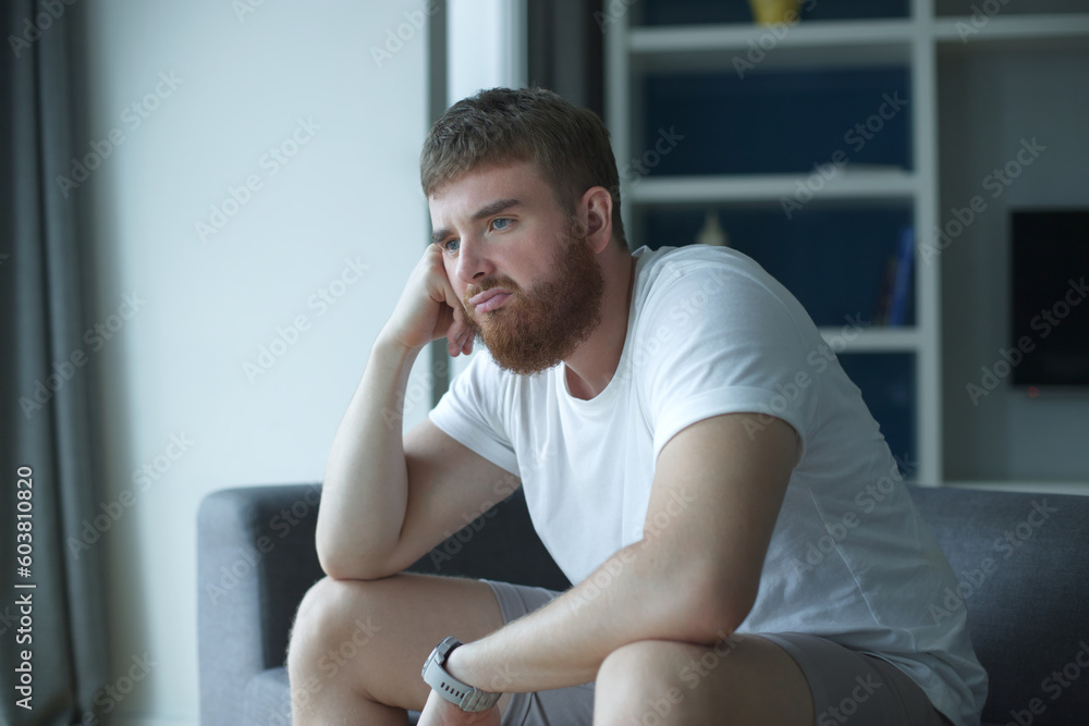 Depressed unhappy middle-aged sad man sitting on couch in living room, leaning on his hands, having troubles loneliness, home interior, holding his forehead while having a headache