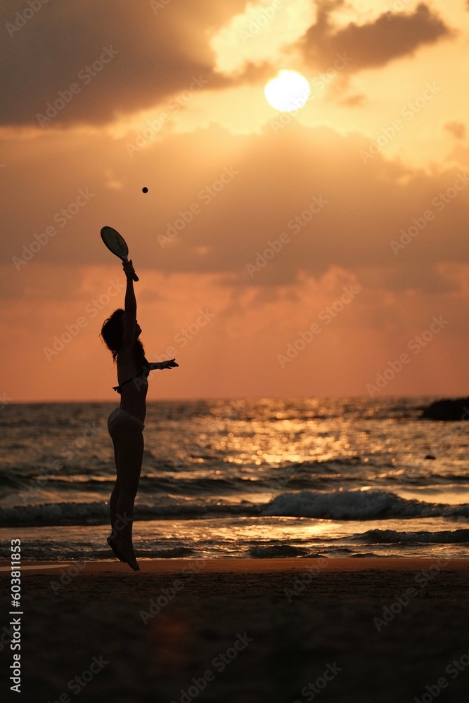 09.18.2022. Tel Aviv. Israel. A girl plays a ball with a racket and jumps on the beach in Tel Aviv at sunset