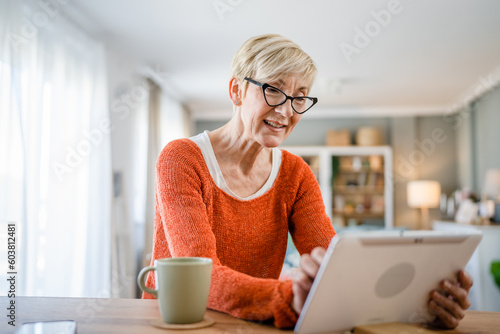 One senior blonde woman use digital tablet for video call at home