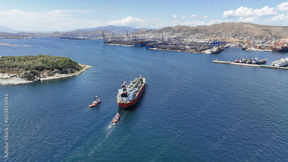 Aerial drone photo of huge crude oil tanker assisted by tug boats cruising near container terminal of Perama, Piraeus, Attica, Greece
