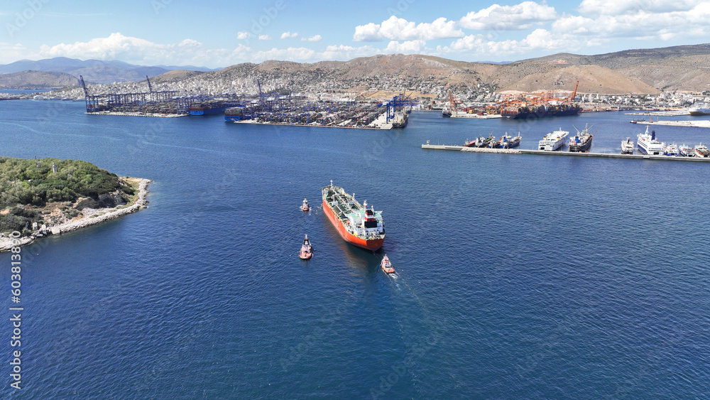 Aerial drone photo of huge crude oil tanker assisted by tug boats cruising near container terminal of Perama, Piraeus, Attica, Greece