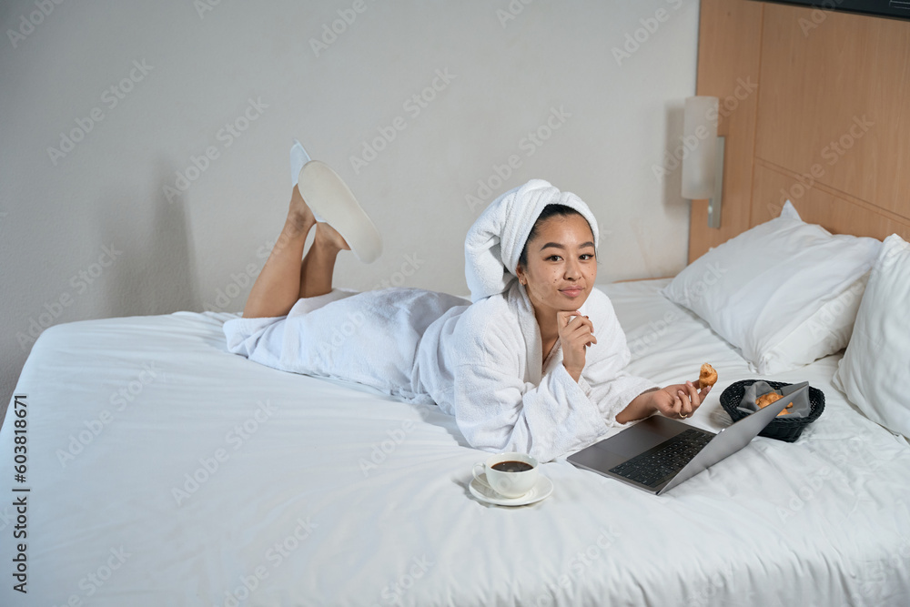 Woman in bathrobe using laptop is having breakfast on bed Woman in bathrobe using laptop is having breakfast on bed