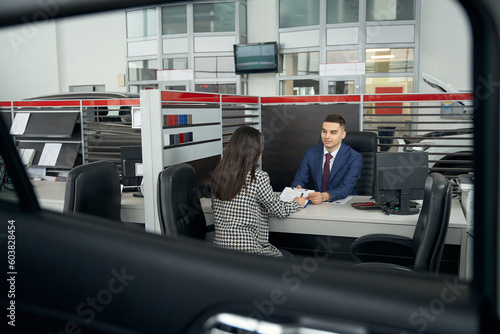 Young brunette woman and car dealership manager communicate in office area