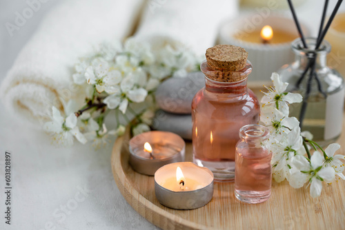 Aromatherapy, home decor concept. Glass perfume bottle, elegant composition with spring flowers. Burning candles, spa setting, essential oils, organic pure aromatic ingredients, atmosphere of relax