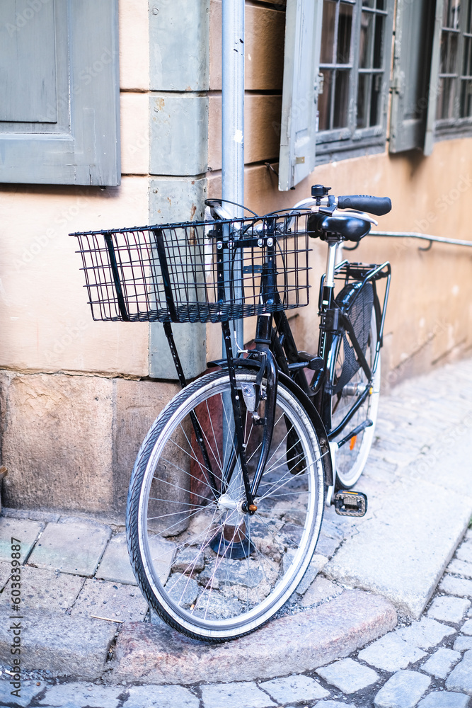 Walking black bicycle with a basket parked to a pillar in the city Walking black bicycle with a basket parked to a pillar in the city