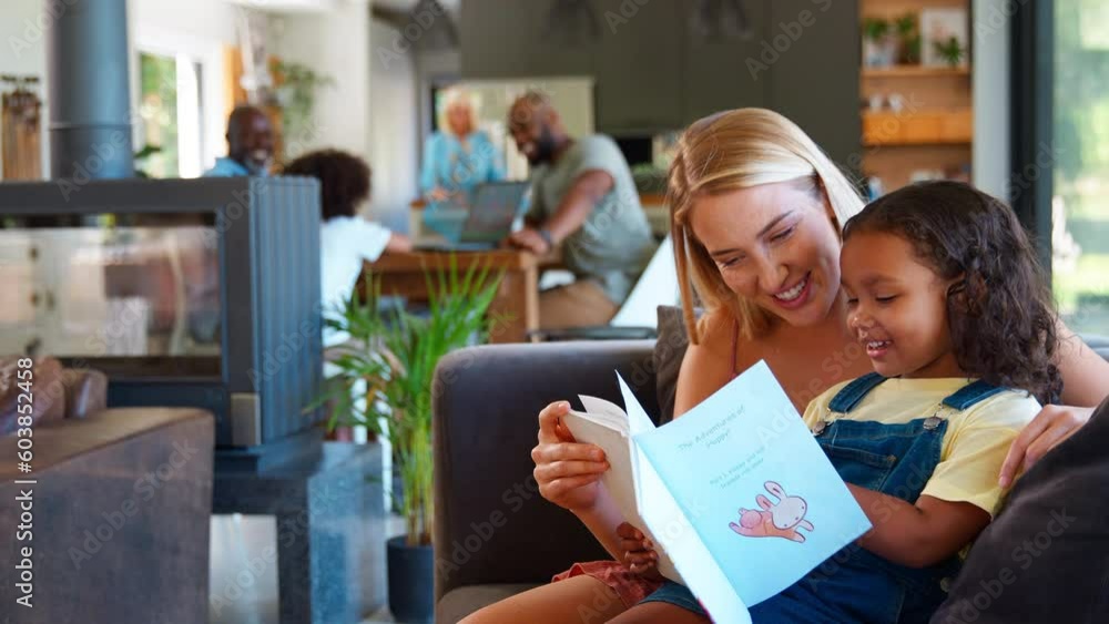 Mother and daughter reading book at home together with multi-generation family in background - shot in slow motion Mother and daughter reading book at home together with multi-generation family in background - shot in slow motion