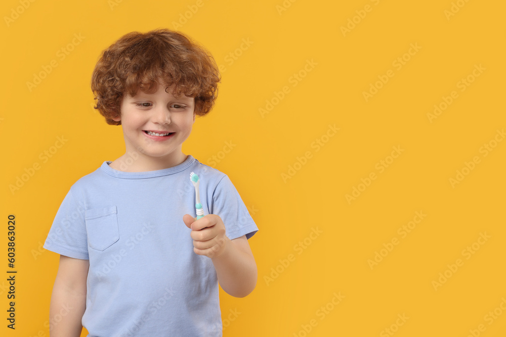 Cute little boy holding plastic toothbrush on yellow background, space for text Cute little boy holding plastic toothbrush on yellow background, space for text