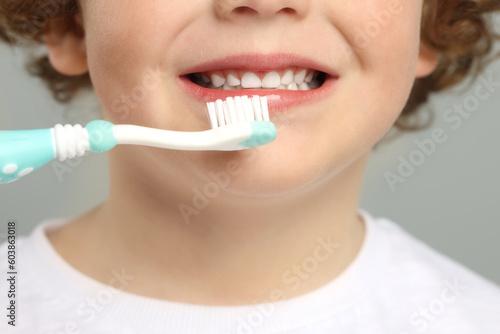 Cute little boy brushing his teeth with plastic toothbrush on light grey background, closeup