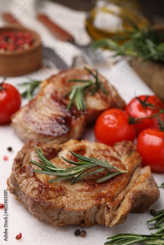 Delicious fried meat with rosemary, tomatoes and spices on white table, closeup