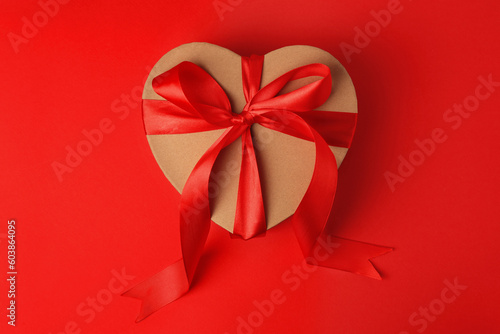 Beautiful heart shaped gift box with bow on red background, top view