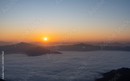 Silhouettes through of beautiful landscape on the mountains at sunrise. Spectacular view in foggy valley covered forest under morning sky.