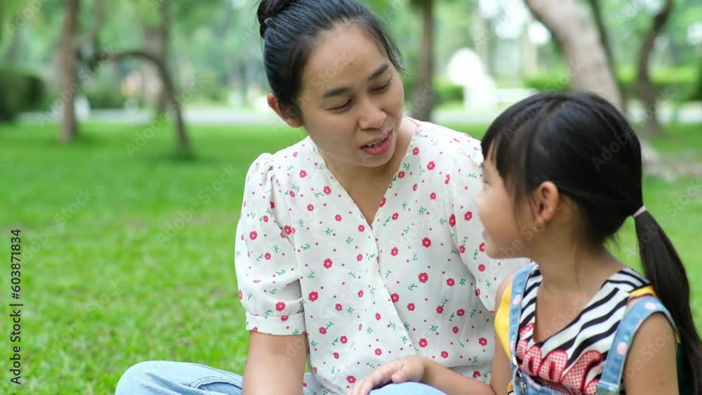 Mother and little daughter sitting on the grass together in the park. Mother having fun with her little daughter outdoors in green nature park. Happy family concept. Mother's Day Mother and little daughter sitting on the grass together in the park. Mother having fun with her little daughter outdoors in green nature park. Happy family concept. Mother's Day