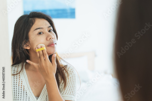 Woman applying makeup concept. Asian woman looking on mirror for applying make up, cosmetic on face by powder puff in morning routine. Cosmetic Make-up make woman more beautiful and self confidence.