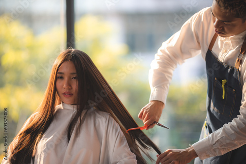 Asian Hairdresser giving treatment and barber occupation service, Professional hairstylist combing and using scissors cut woman's hair to young beautiful customer girl in beauty salon © chokniti