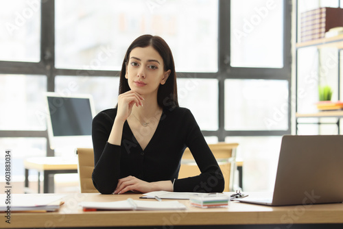 Pretty female worker looks forward at workplace in office