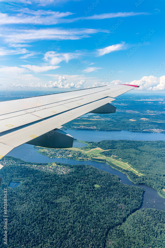 Obraz premium View of airplane wing, blue skies and green land during landing. Airplane window view.