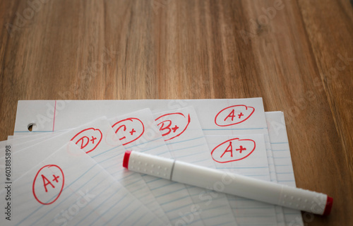 Different grades school paper marked in red ink over a wood desktop. Test results concept. photo