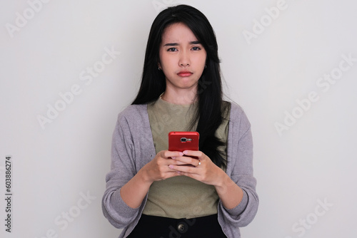 Young Asian woman showing sad expression while texting on her mobile phone photo