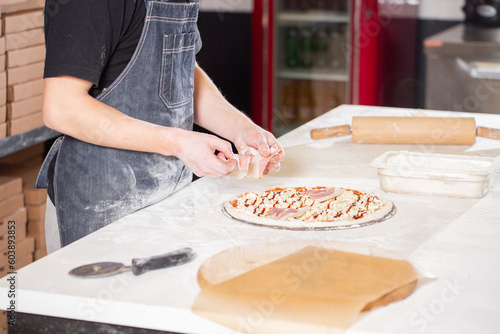 Cooking pizza. arranges cheese ingredients on the dough preform. Closeup hand of chef baker in uniform white apron cook at kitchen