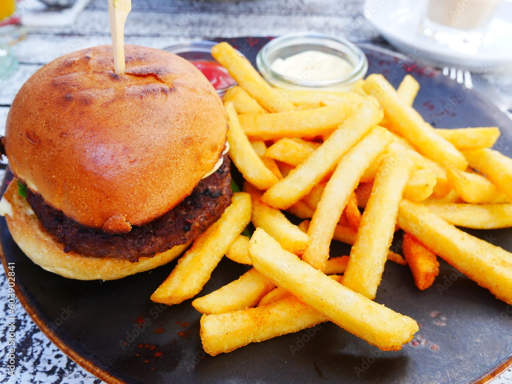 Burger with french fries on wooden table. Hamburger with golden fries served with mayonnaise and ketchup. High-calorie and high-fat fast food. Unhealthy food