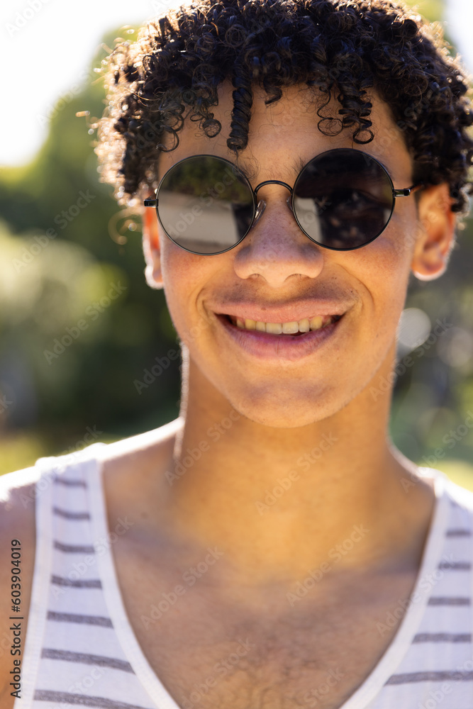 Portrait of smiling biracial fit man wearing vest and sunglasses in sunny garden Portrait of smiling biracial fit man wearing vest and sunglasses in sunny garden