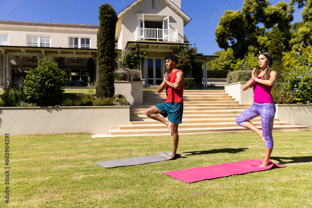 Happy diverse fit couple practicing yoga standing on one leg in sunny garden, copy space